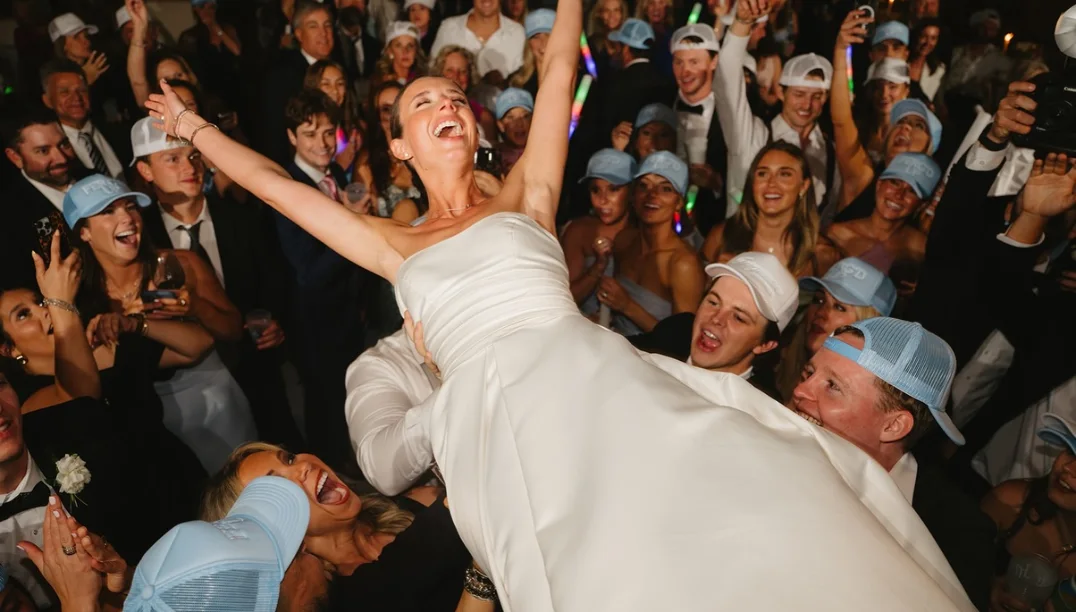 Bride lifted above a cheering crowd of guests in matching hats on the packed dance floor at Grace + Heath's wedding in Texarkana, TX in 2025