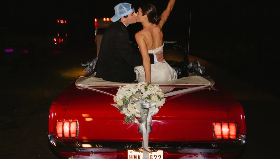 Bride and groom kissing in a red vintage convertible with Texas plates during their send-off at Grace + Heath's wedding in Texarkana, TX in 2025