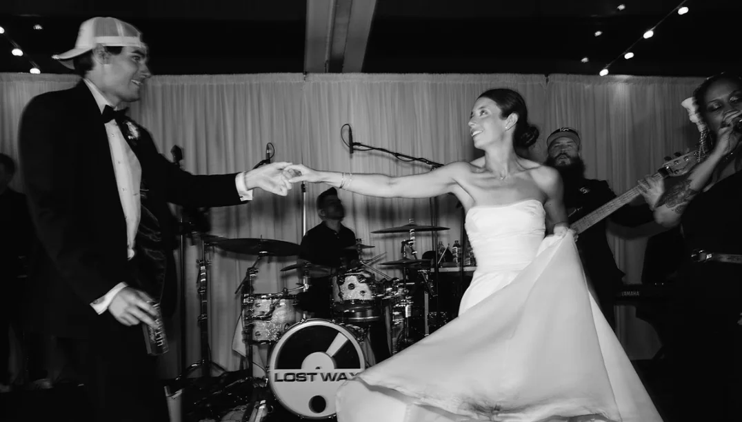 Black-and-white photo of the bride twirling with the groom in front of the Lost Wax band and drum kit at Grace + Heath's wedding in Texarkana, TX in 2025